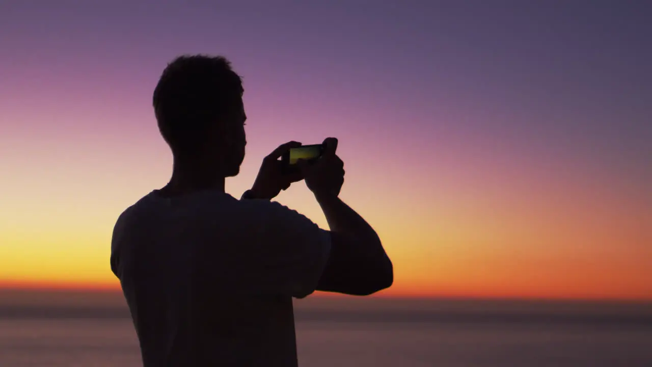 Man taking panorama photo with phone on a beach at sunset