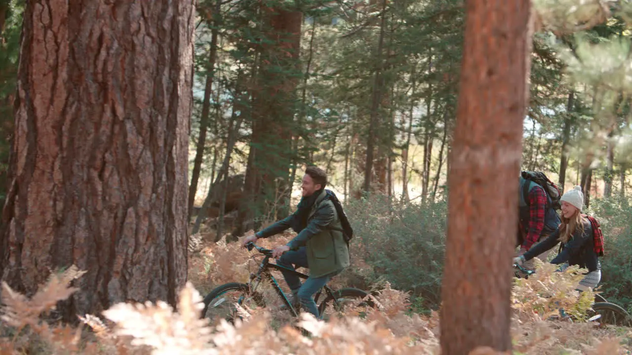 Friends riding bikes in forest side view right to left pan