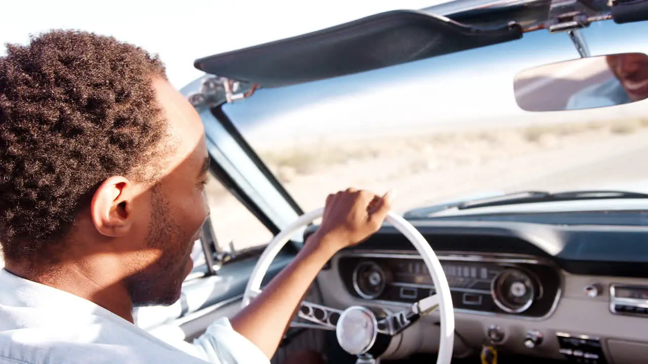 Black man driving open top car on desert highway close up