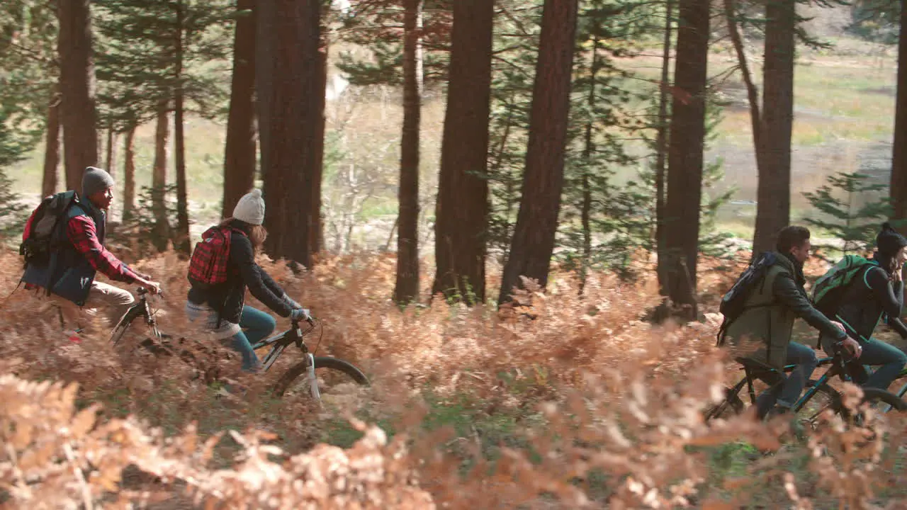 Friends riding bikes in forest side view left to right pan