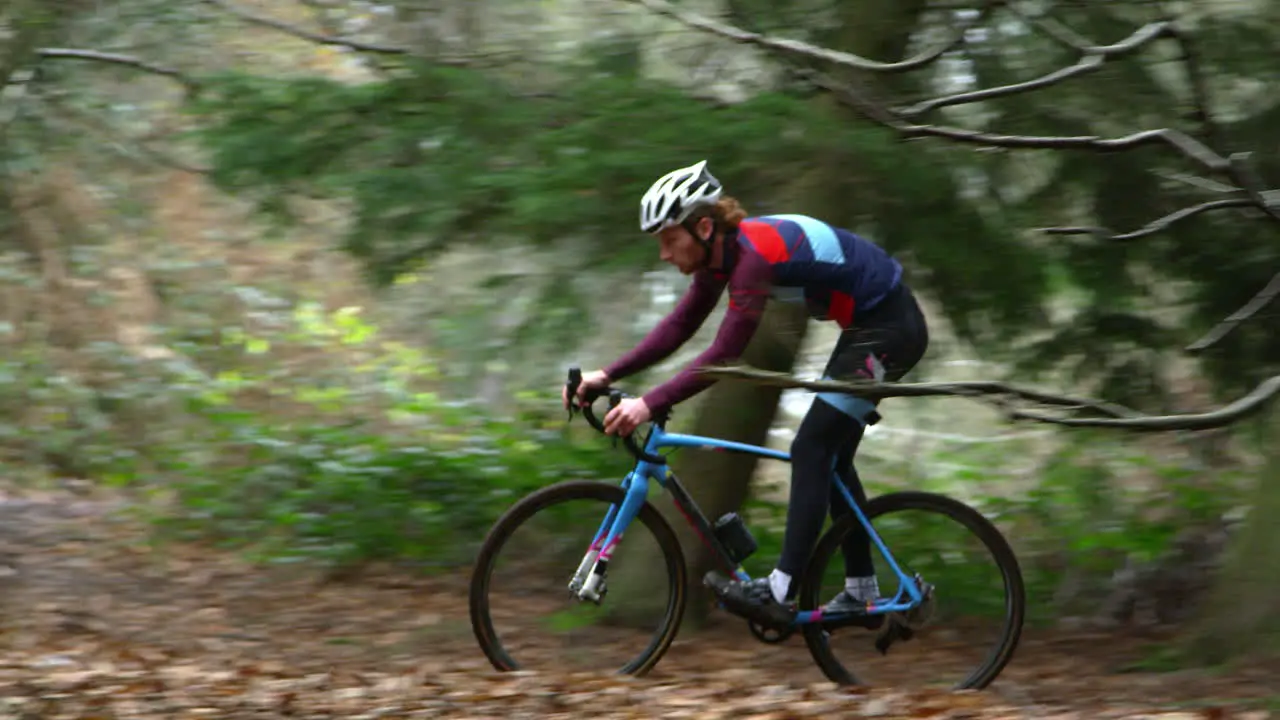 Young man cross-country cycling between trees in a forest shot on R3D