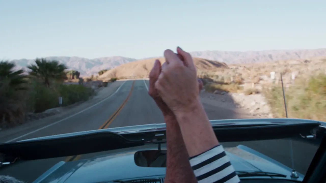 Senior couple hold hands in the air driving in open top car