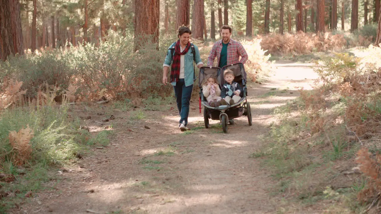 Male parents pushing stroller with two kids through a forest