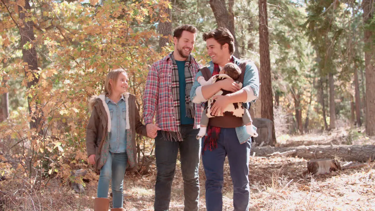 Male parents in forest with baby and daughter walk to camera