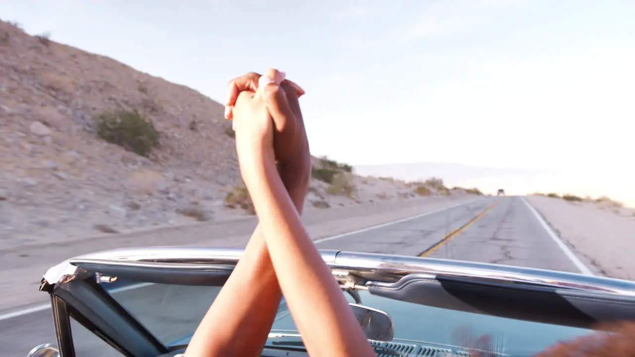 Young black couple in open top car holding hands in the air