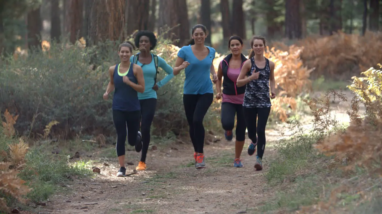 Group of young adult women running in a forest slow motion