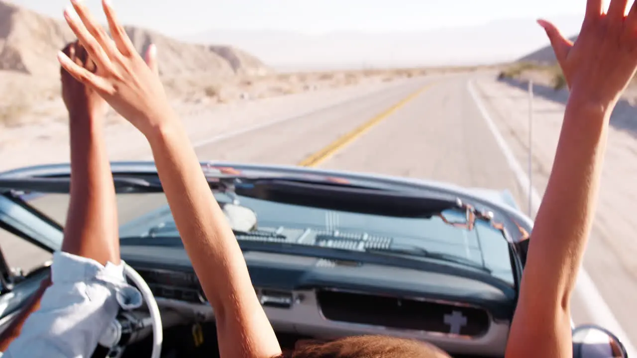 Couple driving open top car raising their hands in the air