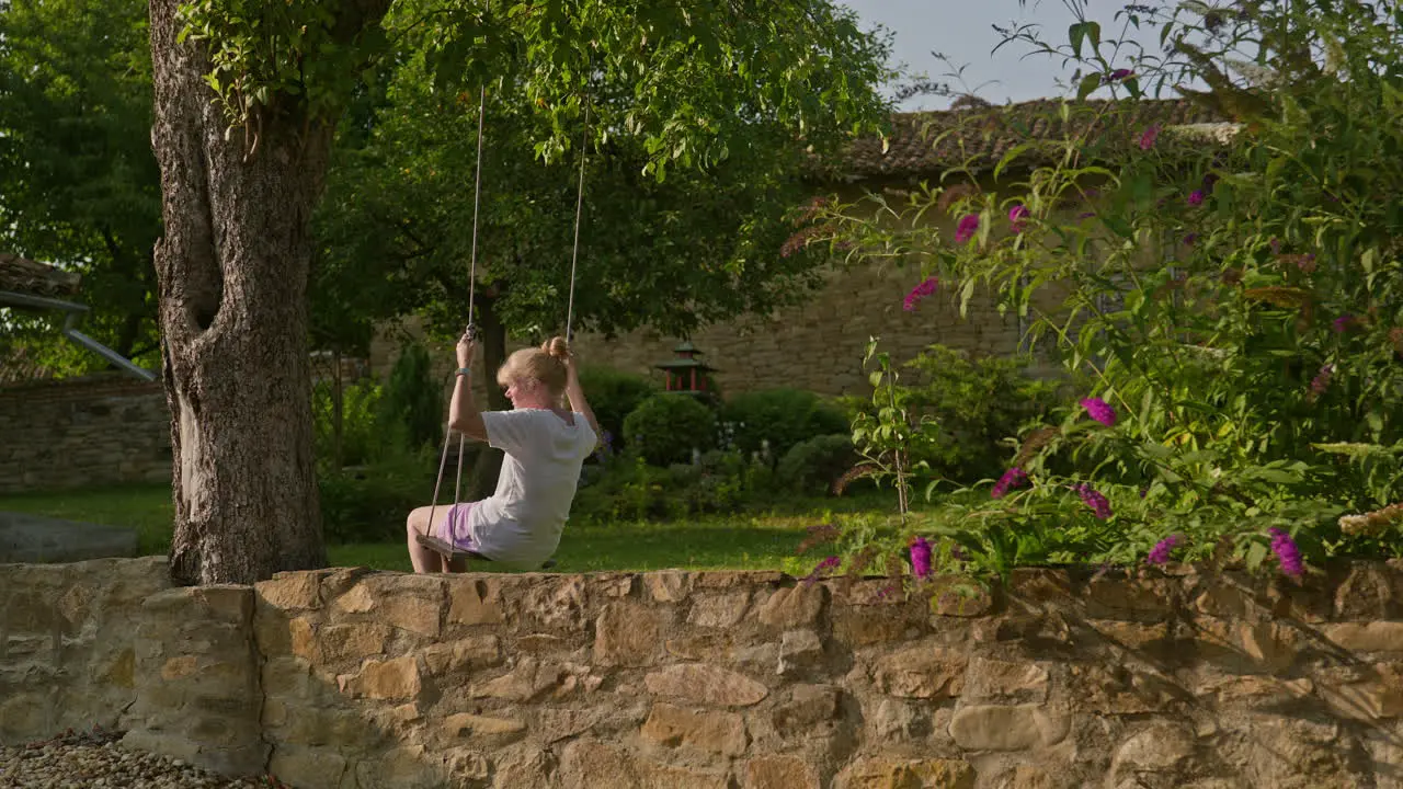 Woman on tree swing enjoys peaceful solitude of garden on summer morning