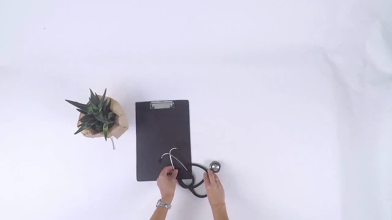 Top-down view of medical items placed on white background with a stethoscope syringe black dossier folder white glasses and small plants