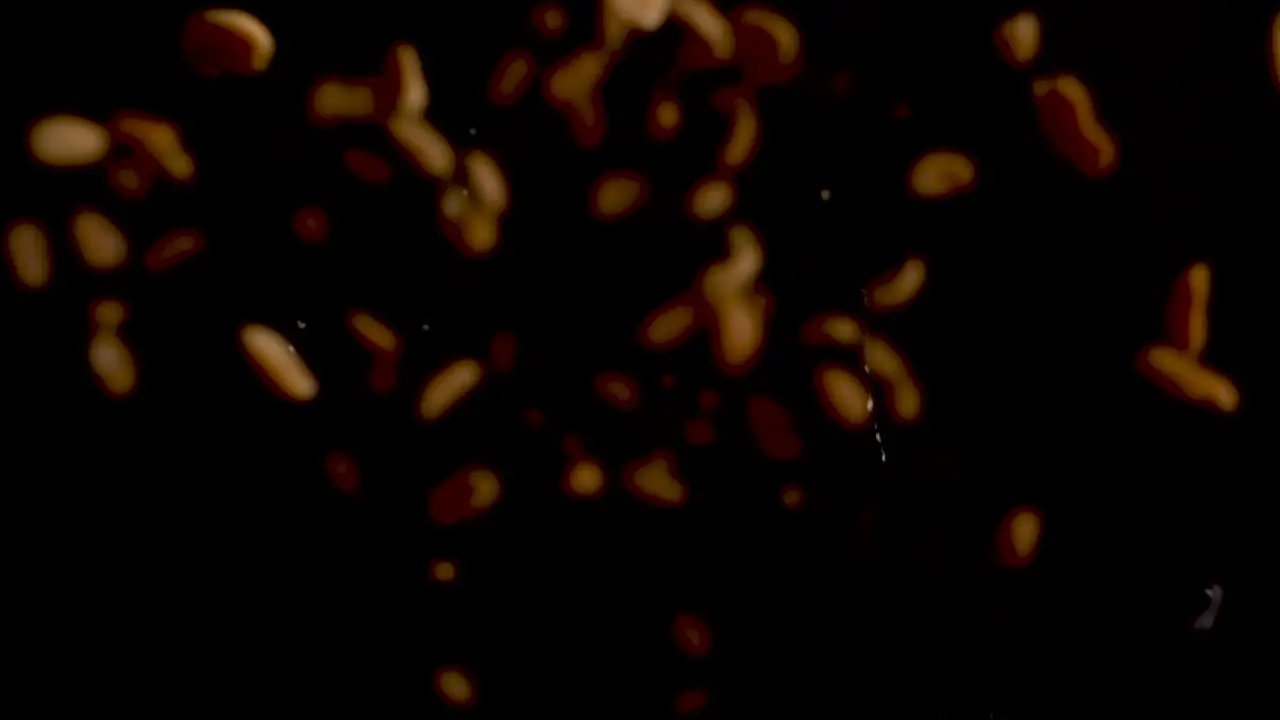 Many illuminated peanuts falling towards lens and falling down on black surface