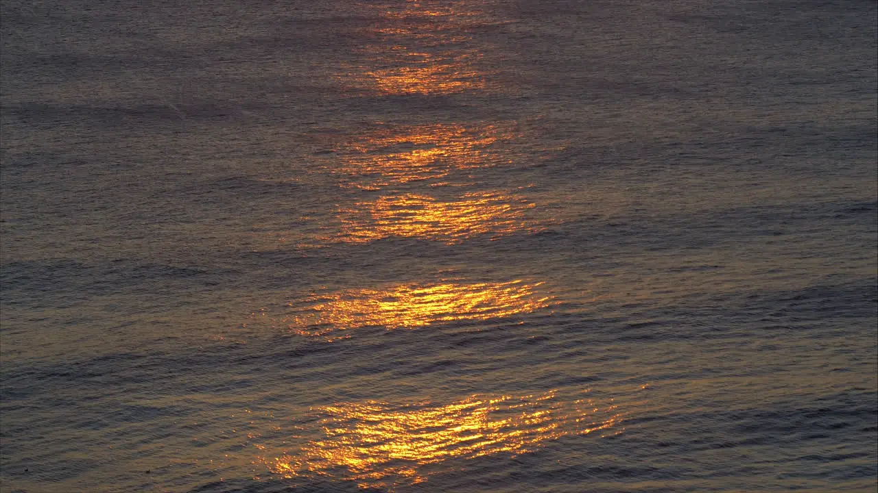 Sunset casts shimmering orange glow across ocean waves