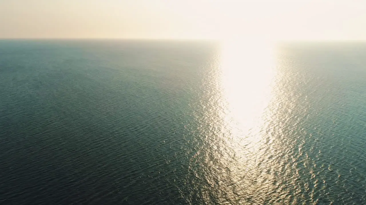 High Aerial Drone Shot into the Sun of Stunning Beautiful Sunset Over Calm Still Sea with Small Waves