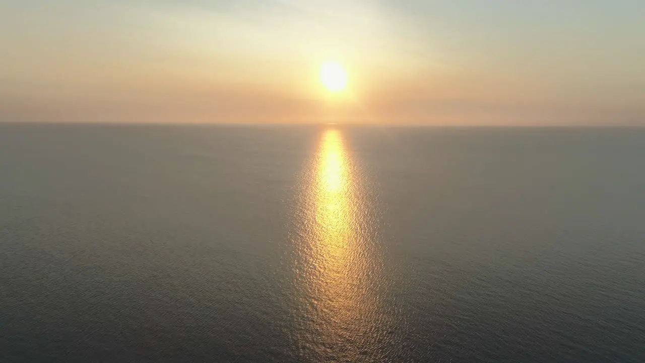 High Aerial Drone Shot of Beautiful Stunning Sunset at Golden Hour Over the Sea into the Sun with Amazing Reflection with Small Waves and Calm Sea in UK