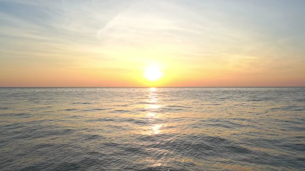 A pink and orange sunset forms under a bright setting sun