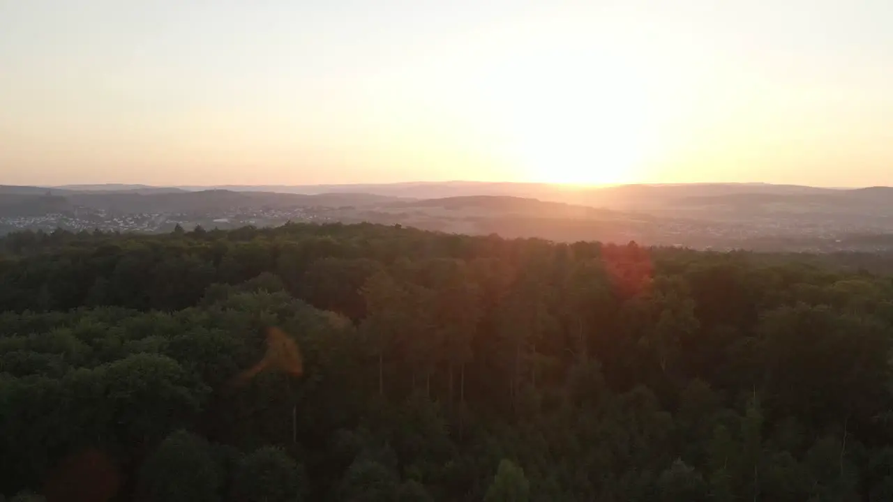 Rising drone footage over a huge forest at an orange sunset with mountains in the background