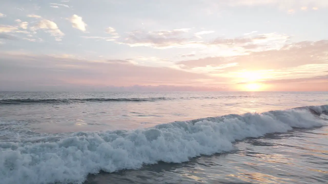 Aerial slow motion shot of the white foaming surf of the pacific ocean under a beautiful orange sunset in costa rica