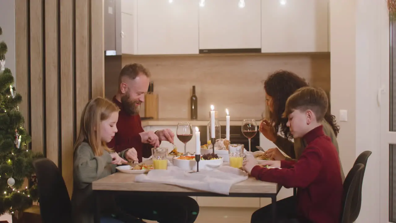 Family Of Parents And Two Siblings Having Dinner At Christmas Sitting At The Kitchen Table