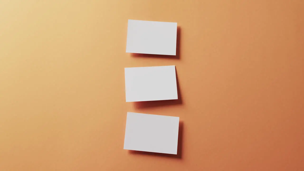 Overhead view of three white business cards arranged on orange background copy space slow motion