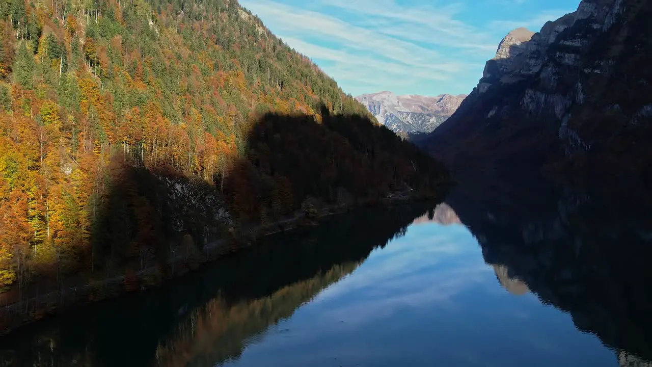 Aerial Dolly Over Calm Reflective Lake In With Autumnal Forest Trees On Valley Hillside