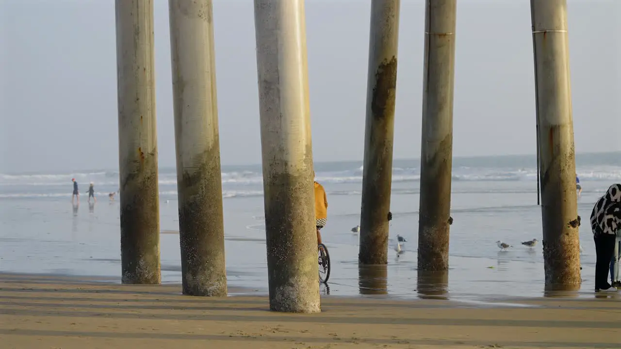 Tall skinny caucasian man riding a bike on the beach under the pier