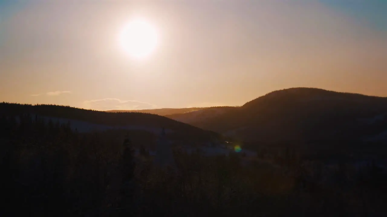 Beautiful orange sunlight at sky over snowy mountain range silhouette in Norway Wide shot