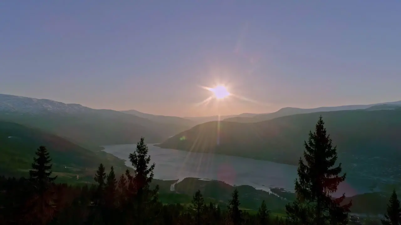 Aerial drone forward moving shot over Norwegian fjord as sun rising from behind beautiful mountain range in Norway during morning time