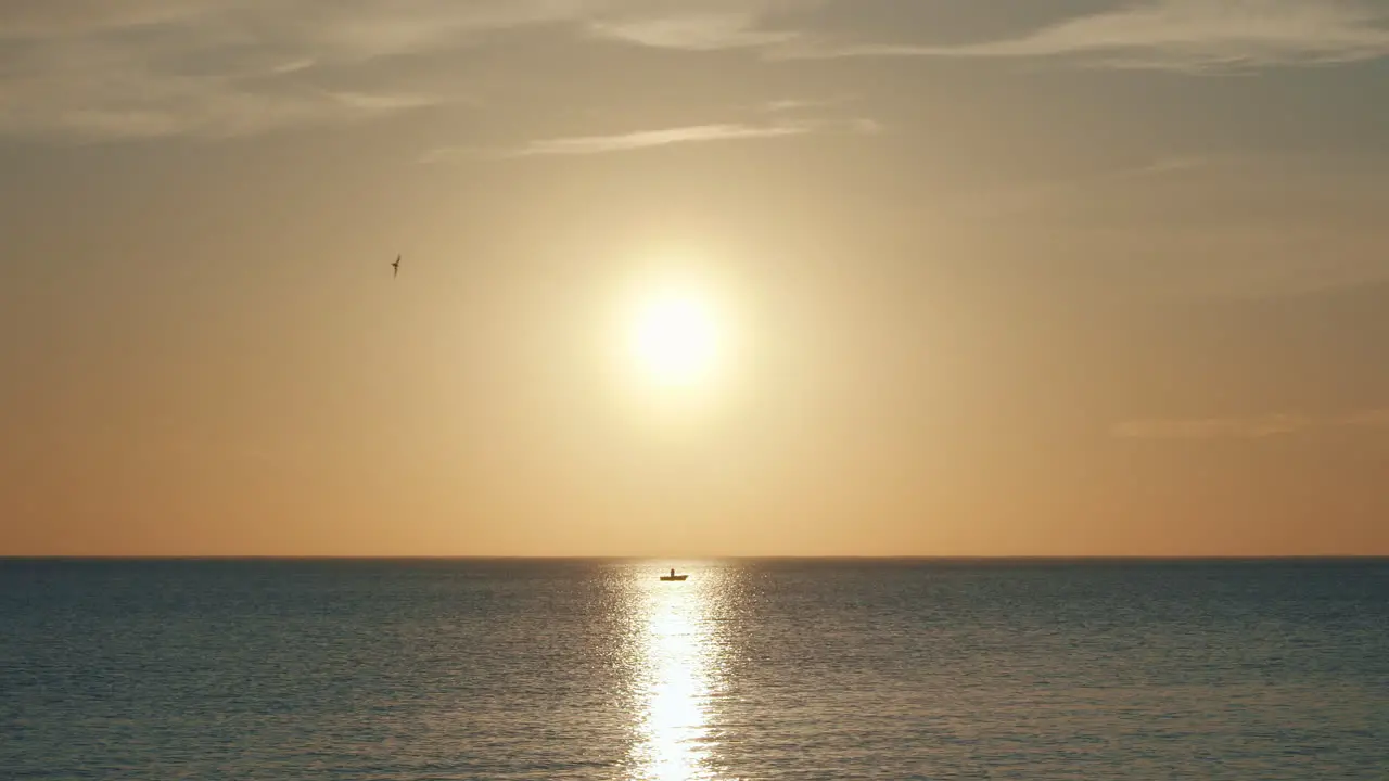 Lonely boat sits at sea during sunset in sun's reflection long shot