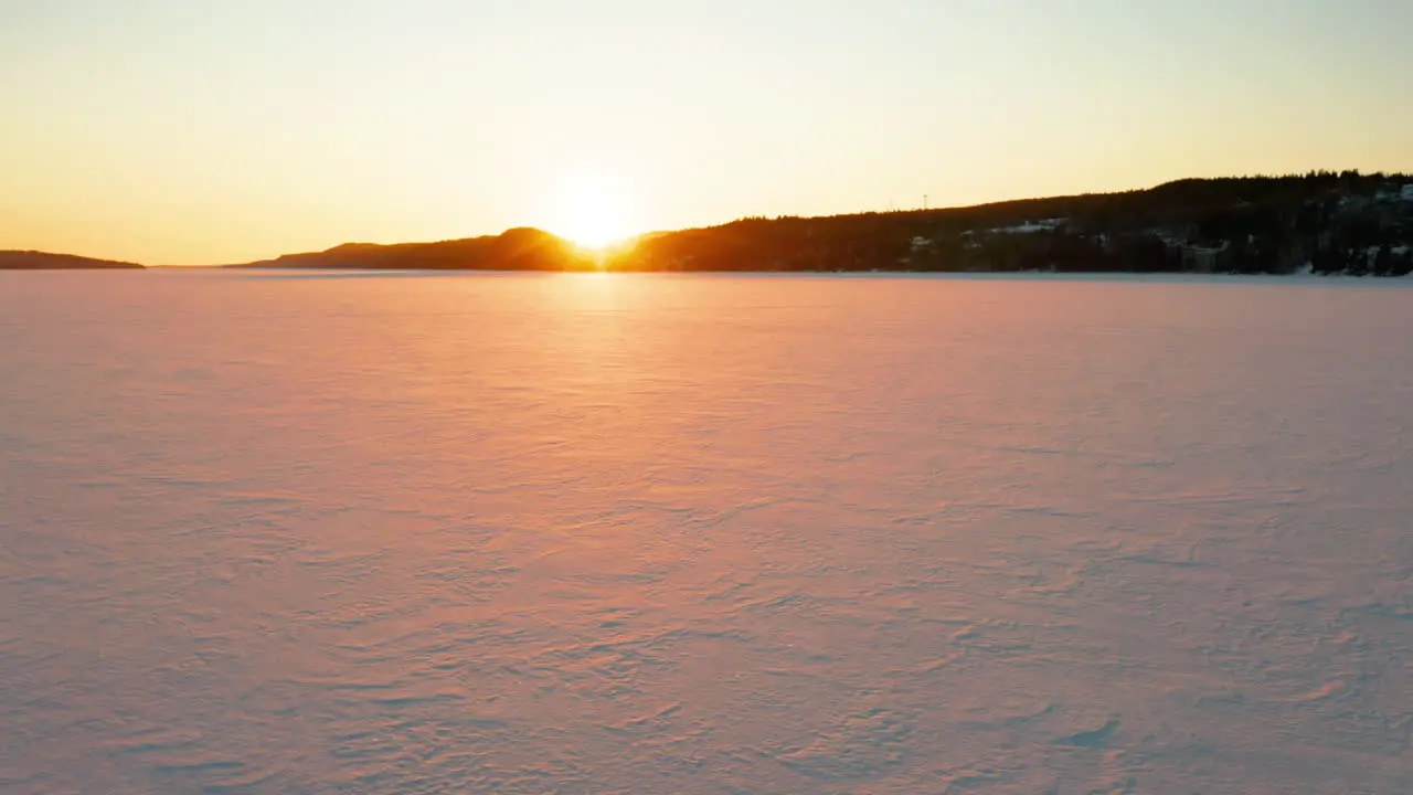 Scenic aerial flying across a frozen lake as the sun sets in the distance