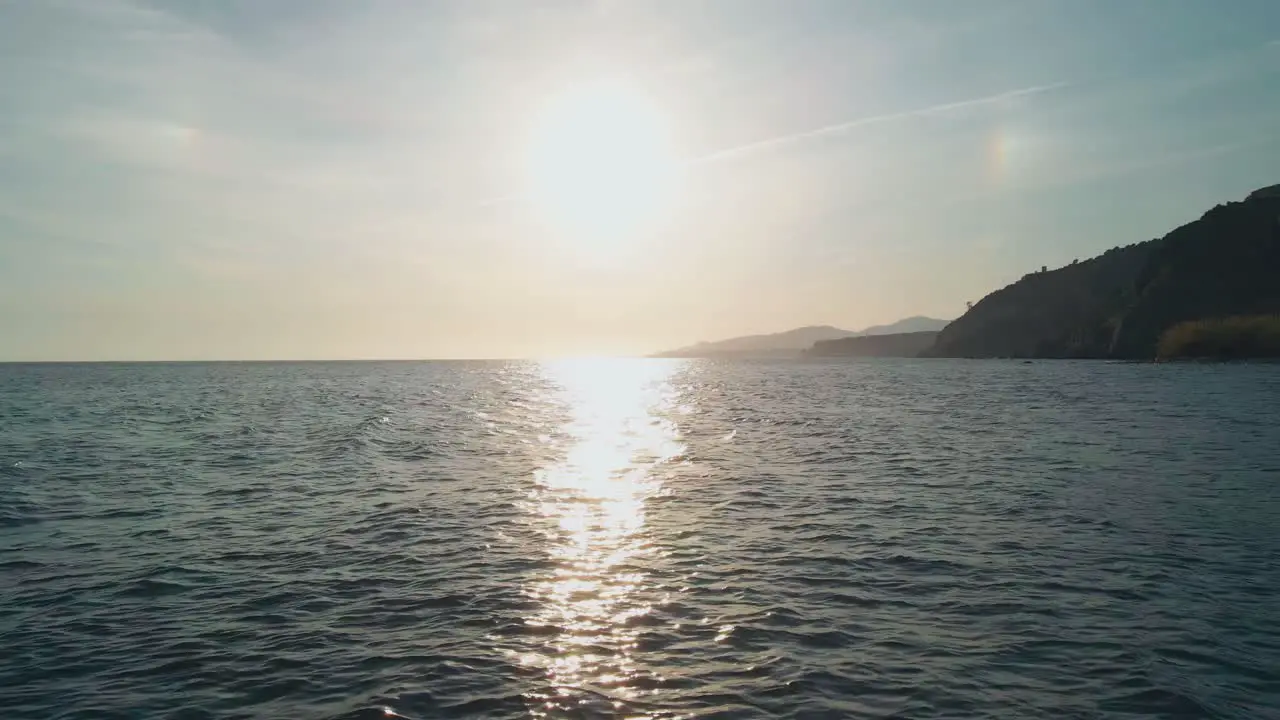 Bright sun over the sea aerial drone moving backwards to the rocky beach