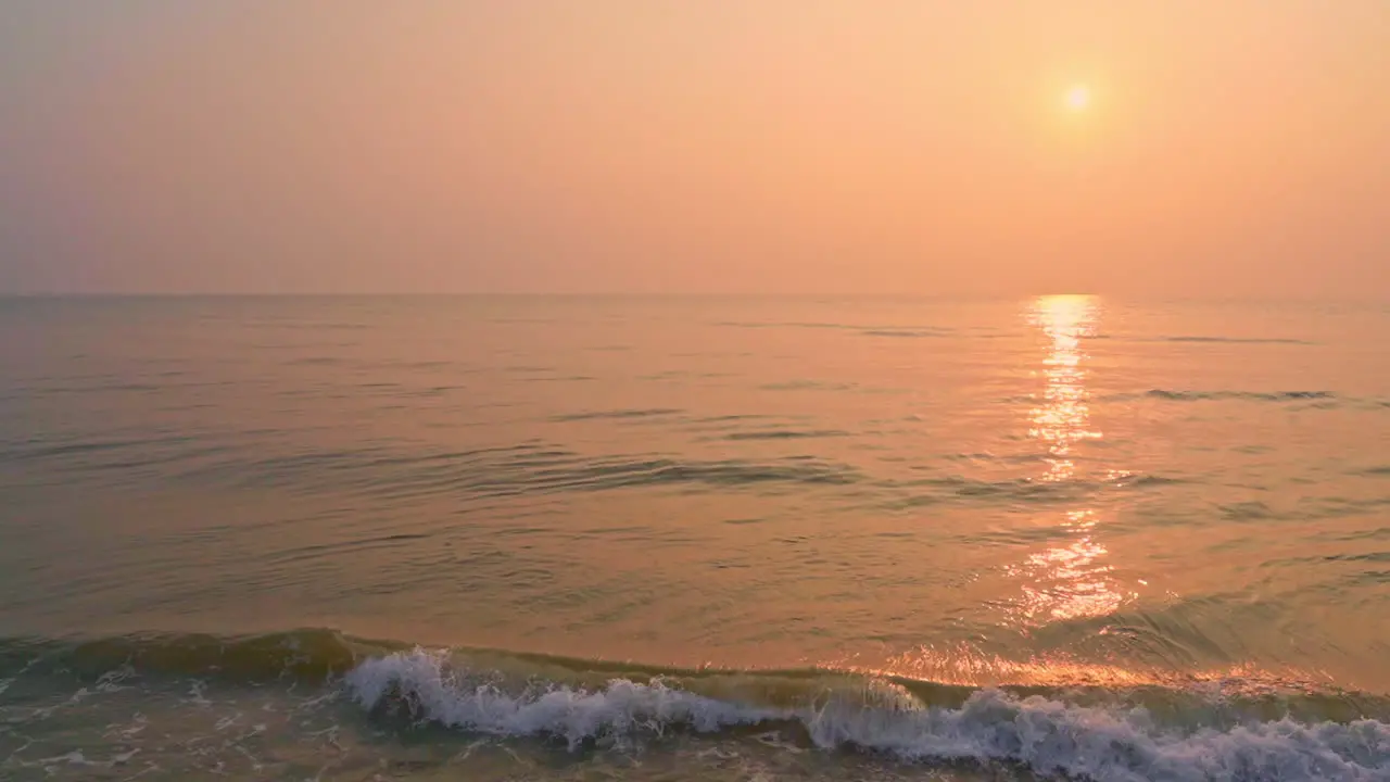 Slowmotion on beautiful pink golden seaside sunset sun reflections on sea tides slowly coming towards beach