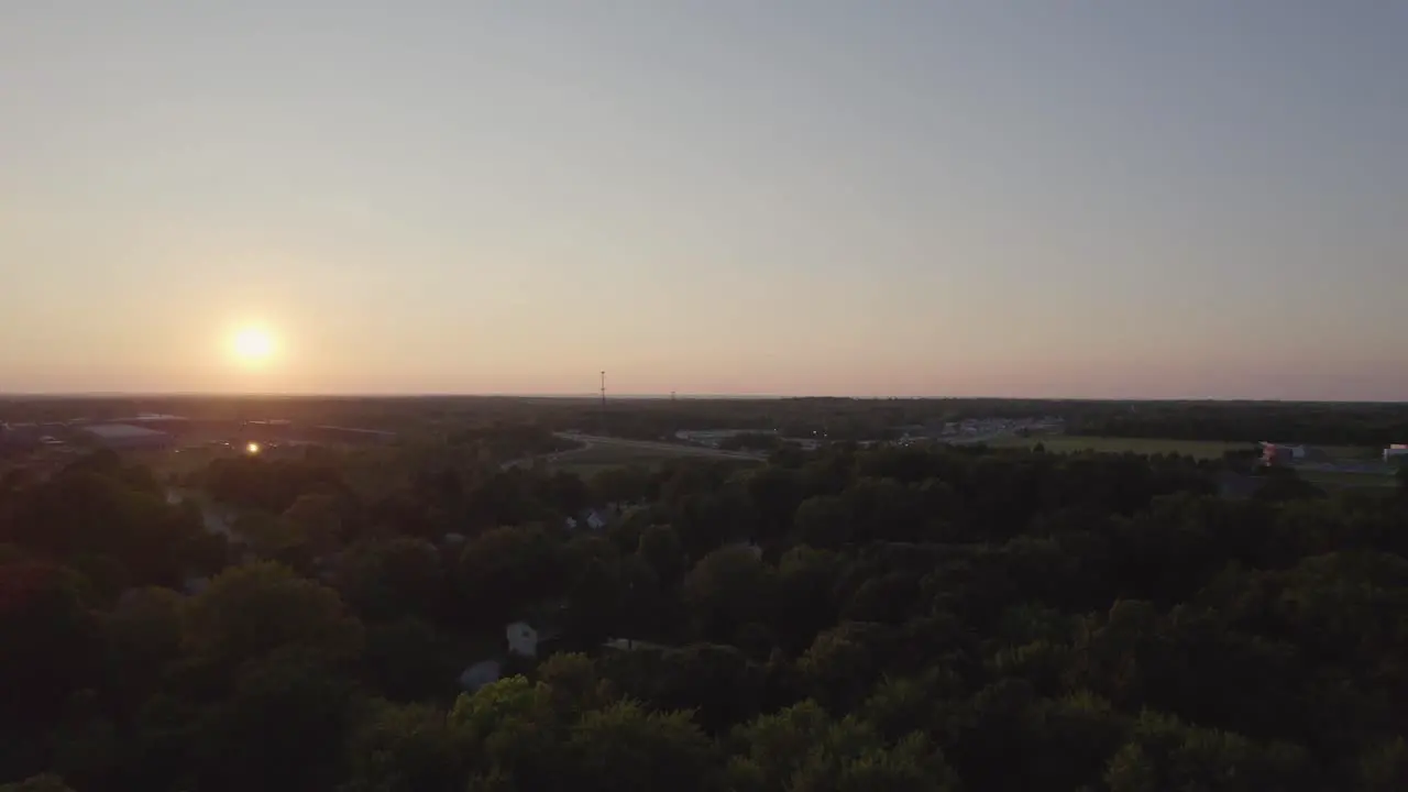 Aerial drone forward moving shot over road network through a small town surrounded by dense vegetation at sunset