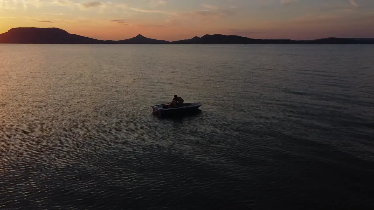 Aerial view of a Young Couple in a Boat Floating on Lake at Sunset with Mountains in the Background