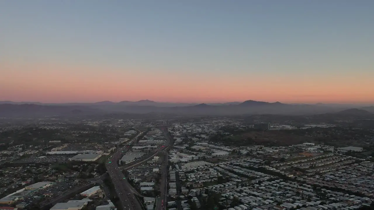 A panning drone shot captures a beautiful sunset over the city with the moon visible in the distance