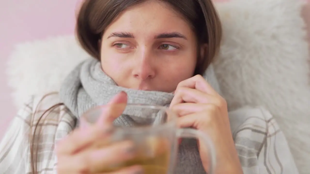 sick girl lying in bed coughing and sniffing girl drinks tea wrapped in scarf