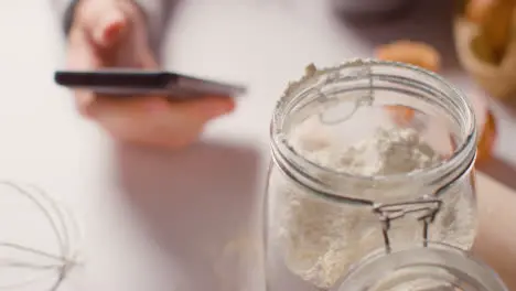 Close Up Of Messy Kitchen Surface With Ingredients And Utensils And Person Using Mobile Phone