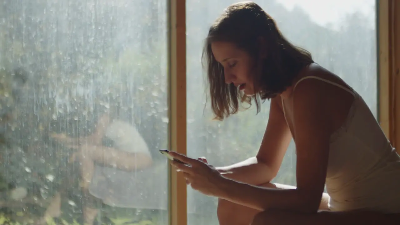 A young half-naked woman sitting on a bed in the morning sun texting on her cell phone