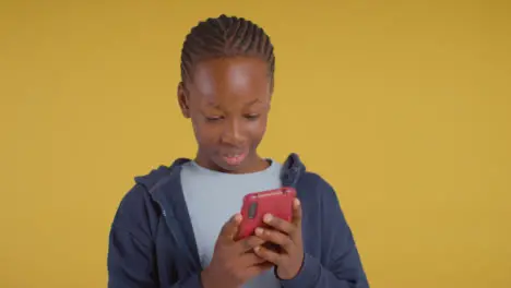 Studio Portrait Of Excited Boy On ASD Spectrum Gaming On Mobile Phone On Yellow Background 2