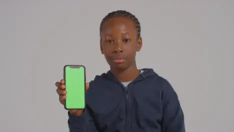 Studio Portrait Of Boy Holding Green Screen Mobile Phone Against Grey Background