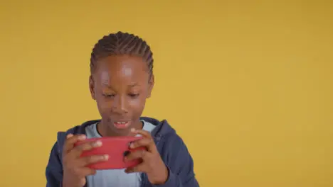 Studio Portrait Of Excited Boy On ASD Spectrum Gaming On Mobile Phone On Yellow Background 1