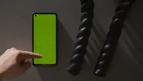 Overhead Studio Fitness Shot Of Person Using Green Screen Mobile Phone Next To Gym Battle Ropes On Grey Background