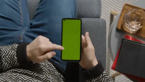 Overhead Shot Of Person At Home Shopping Online Looking At Green Screen On Mobile Phone