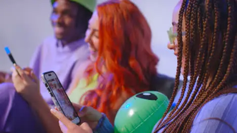 Close Up Studio Shot Of Young Gen Z Friends Sitting On Sofa Talking And Sharing Social Media Post On Mobile Phones 2