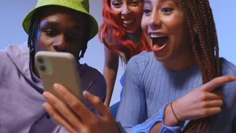 Close Up Studio Shot Of Young Gen Z Friends Sitting On Sofa Sharing Social Media Post On Mobile Phones