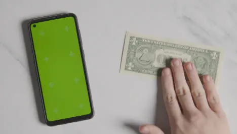 Overhead Currency Shot Of Hand Putting Down US 1 Dollar Bill Next To Green Screen Mobile Phone 