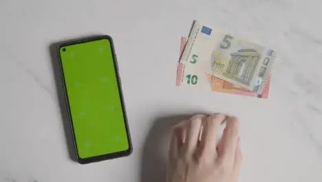 Overhead Currency Shot Of Person Tapping Fingers Next To 10 And 5 Euro Notes And Green Screen Mobile Phone