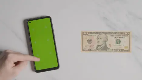 Overhead Currency Shot Of US 10 Dollar Bill Next To Person Using Green Screen Mobile Phone