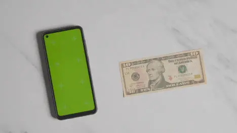 Overhead Currency Shot Of Hand Putting Down US 10 Dollar Bill Next To Green Screen Mobile Phone 