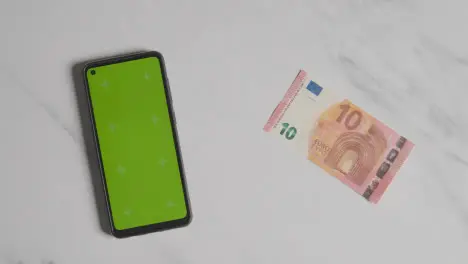 Overhead Currency Shot Of Hand Putting Down US 10 Euro Note Next To Green Screen Mobile Phone 