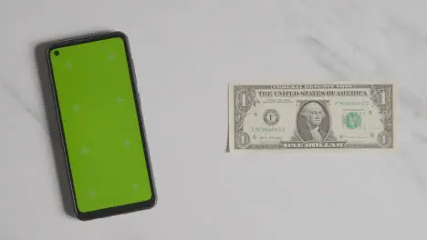 Overhead Currency Shot Of Hand Grabbing US 1 Dollar Bill Next To Green Screen Mobile Phone