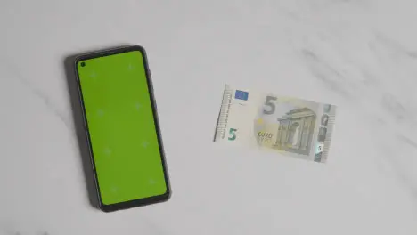 Overhead Currency Shot Of Hand Putting Down US 5 Euro Note Next To Green Screen Mobile Phone 